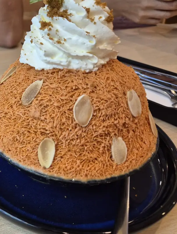 Thai tea bingsu with whipped cream and almond slices on a blue plate