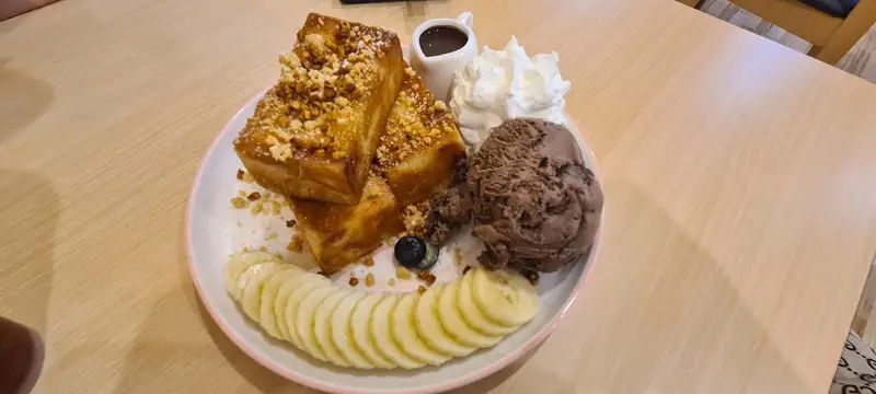 Thick toast with banana slices, chocolate ice cream, cream and a jug of chocolate sauce
